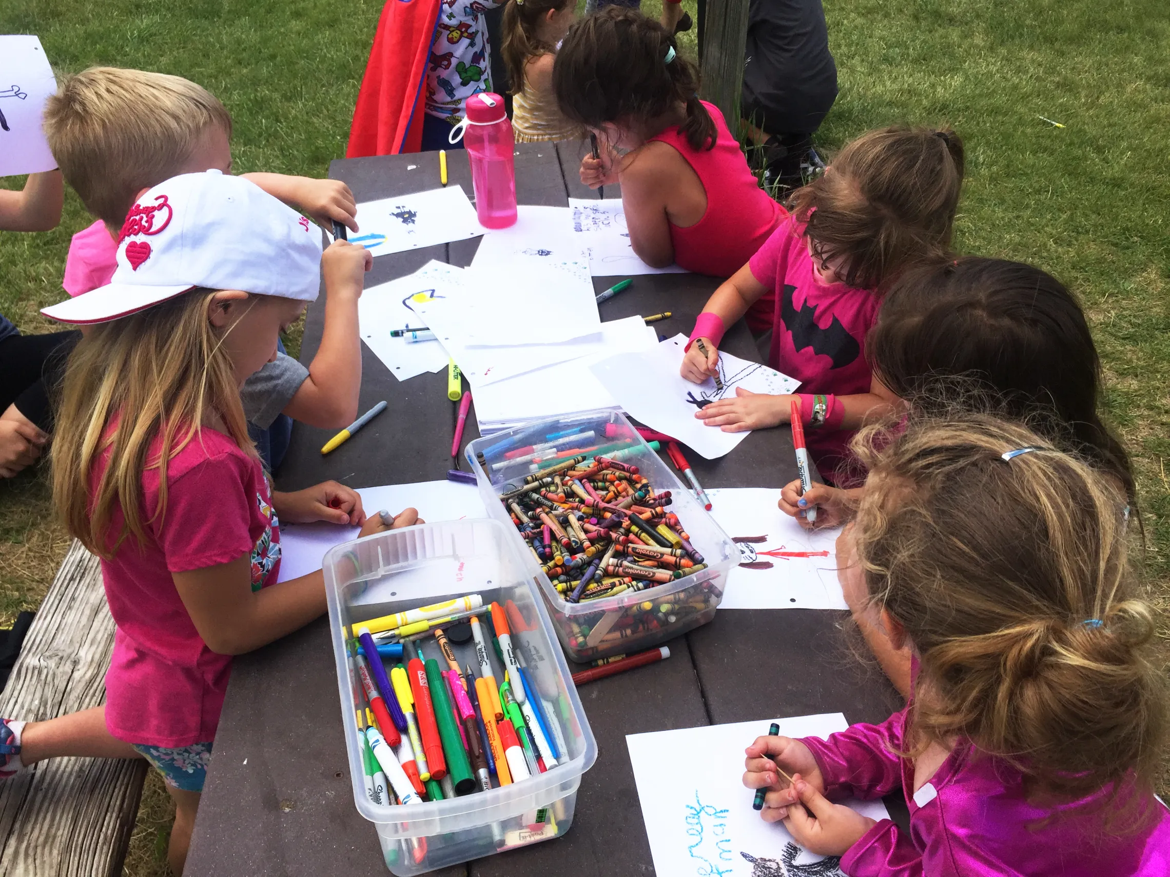 Young students sit outdoors on a bench, coloring.