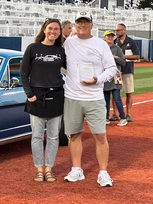 Two individuals stand on a track, holding an award.