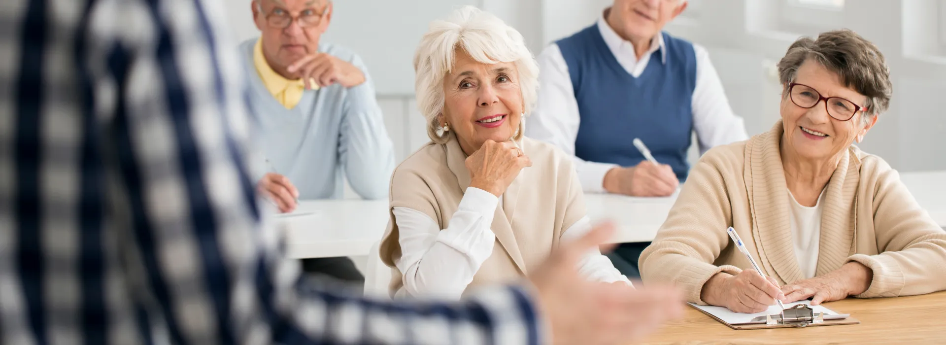 Elderly students sit and take notes as they listen to a presenter