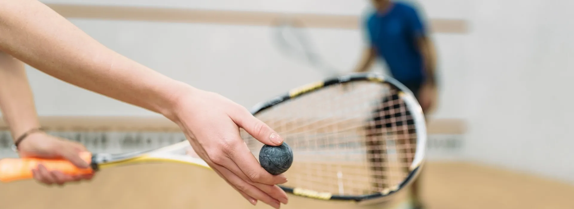 Close up of a hand holding a squash ball and racket, preparing to serve.