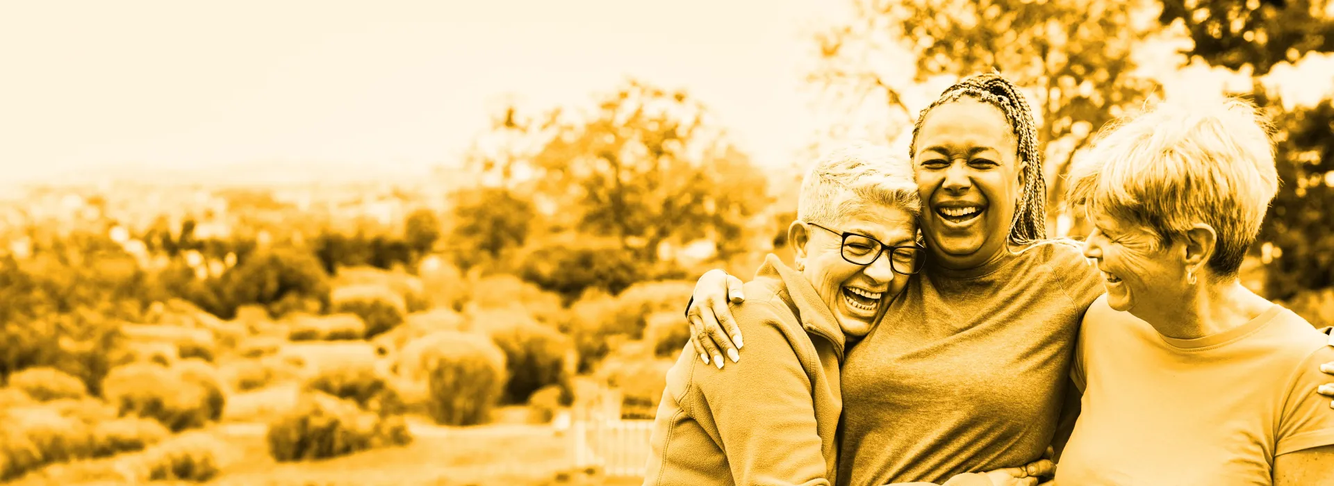 Three friends stand outside, hugging, smiling and laughing.
