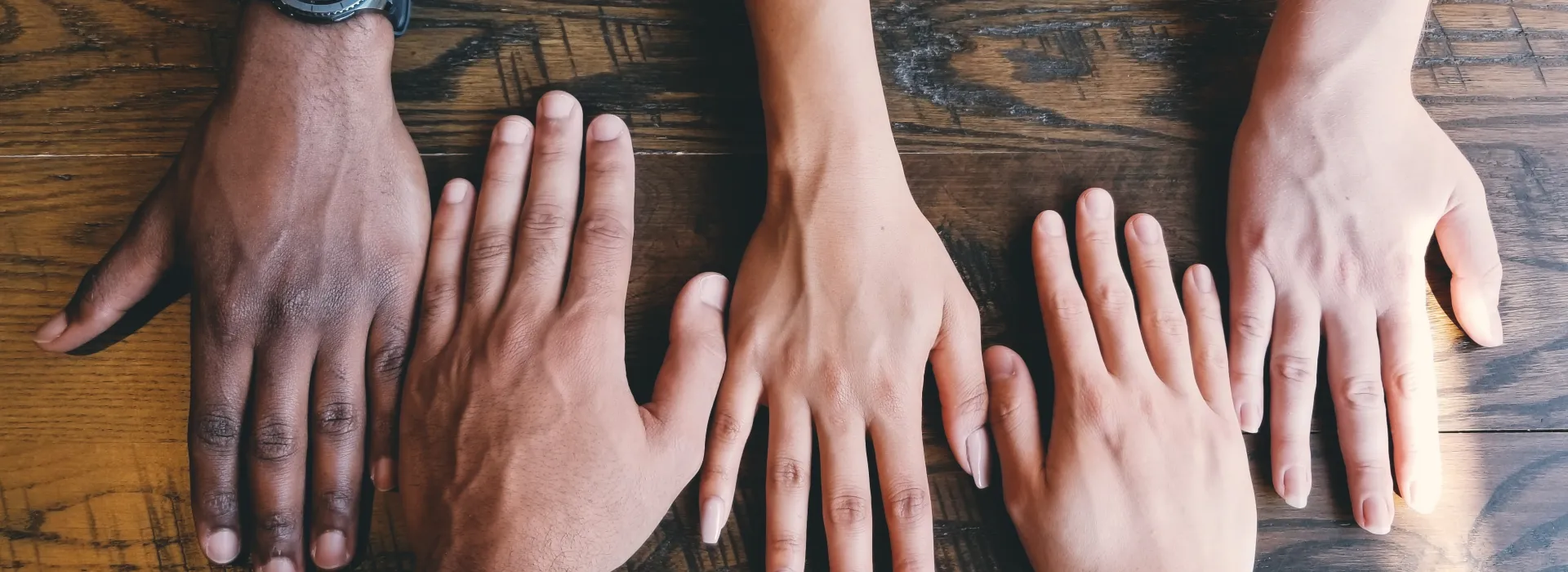 Four sets of hands lay across a dark, grainy wood table, side-by-side