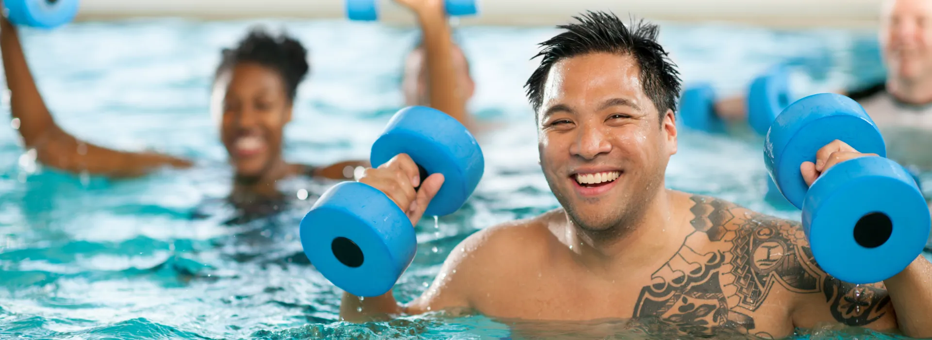 A smiling swim class student lifts blue aquatic fitness weights.