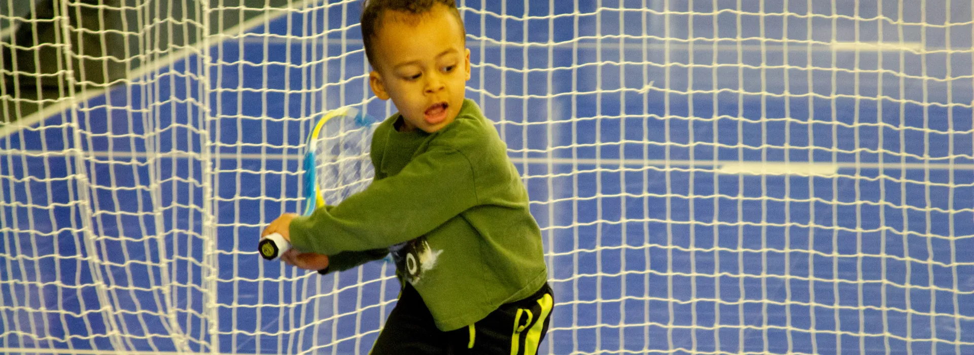 A very young tennis player practices their swing on the court.