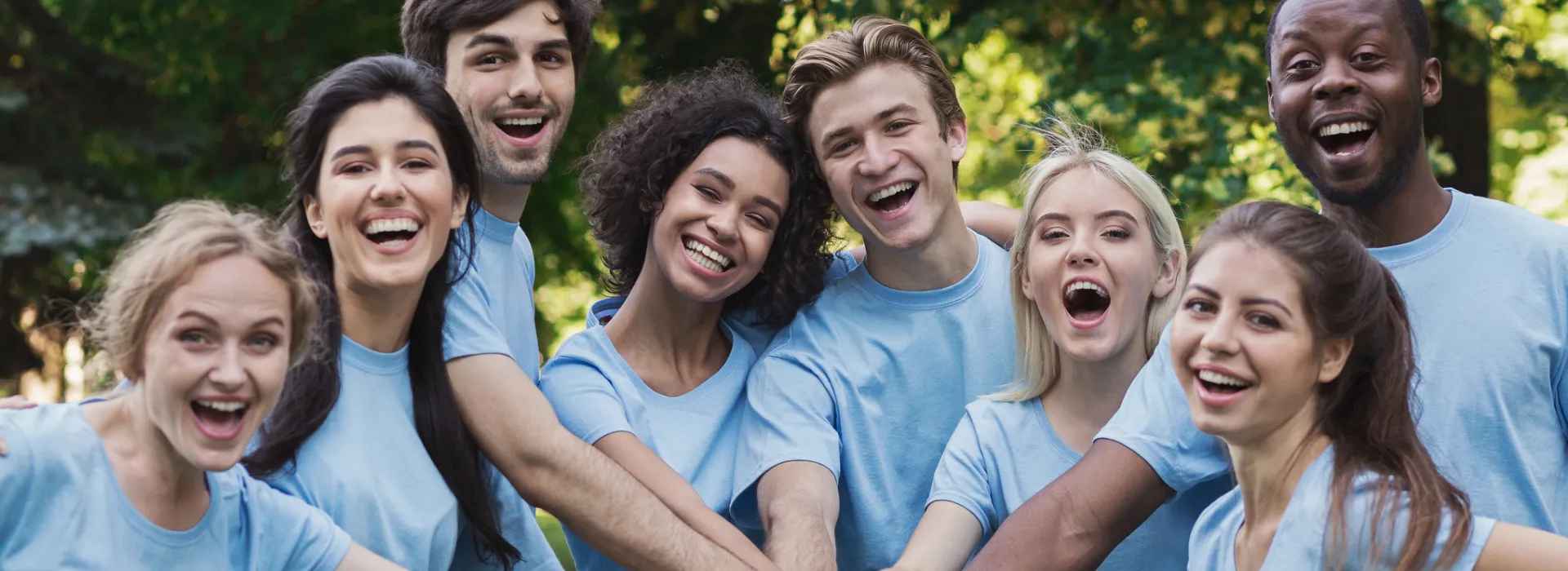 A group of team members wearing matching blue hold hands-in while smiling.
