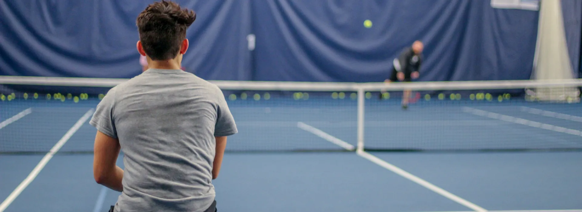 A young tennis player faces his opponent across the court.