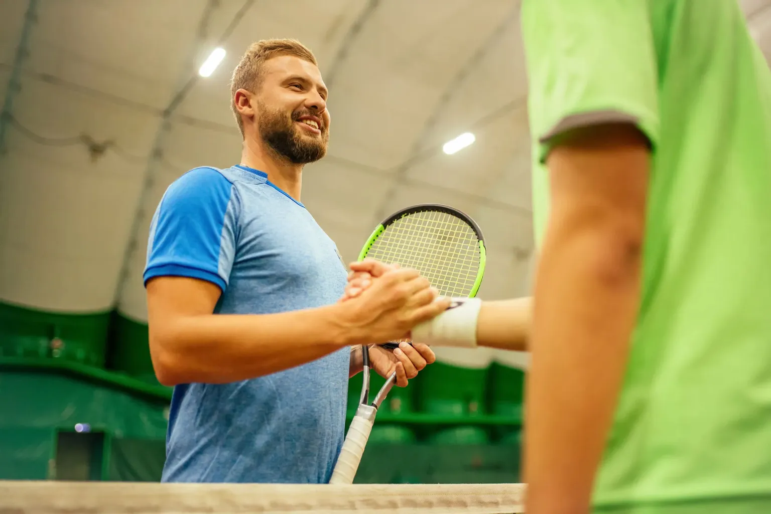 Smiling tennis player shaking hands across the net.