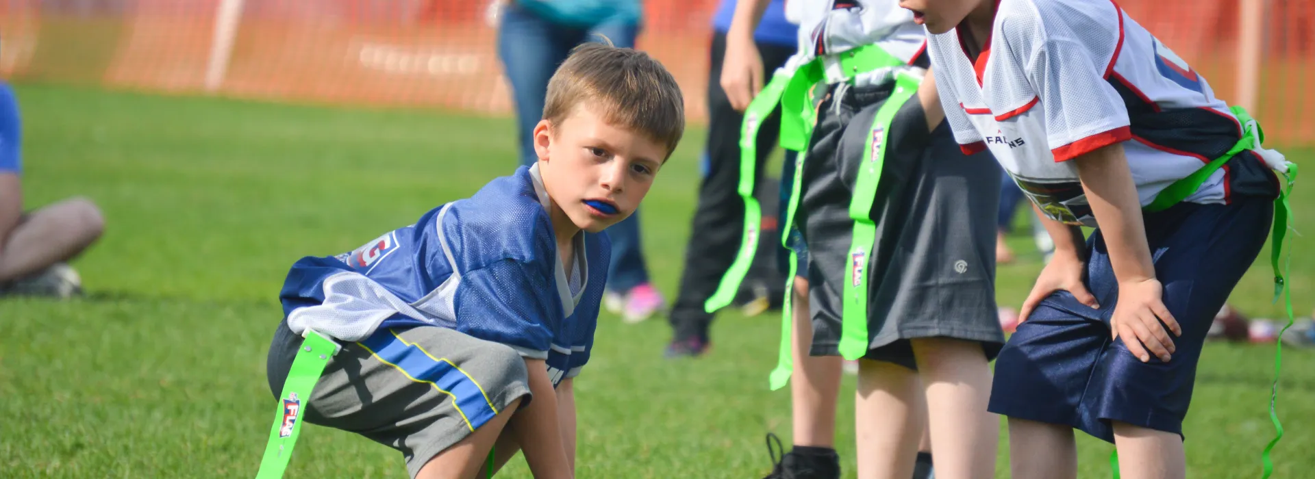 A young flag football player crouches on the field.