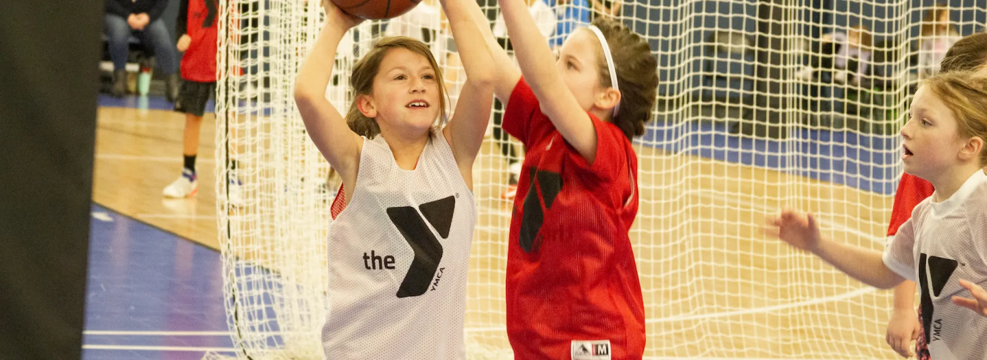 A young basketball player attempts to throw the ball as an opponent rushes to stop them.