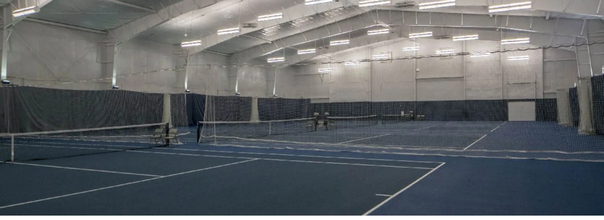 Full room view of multiple well lit, indoor tennis courts