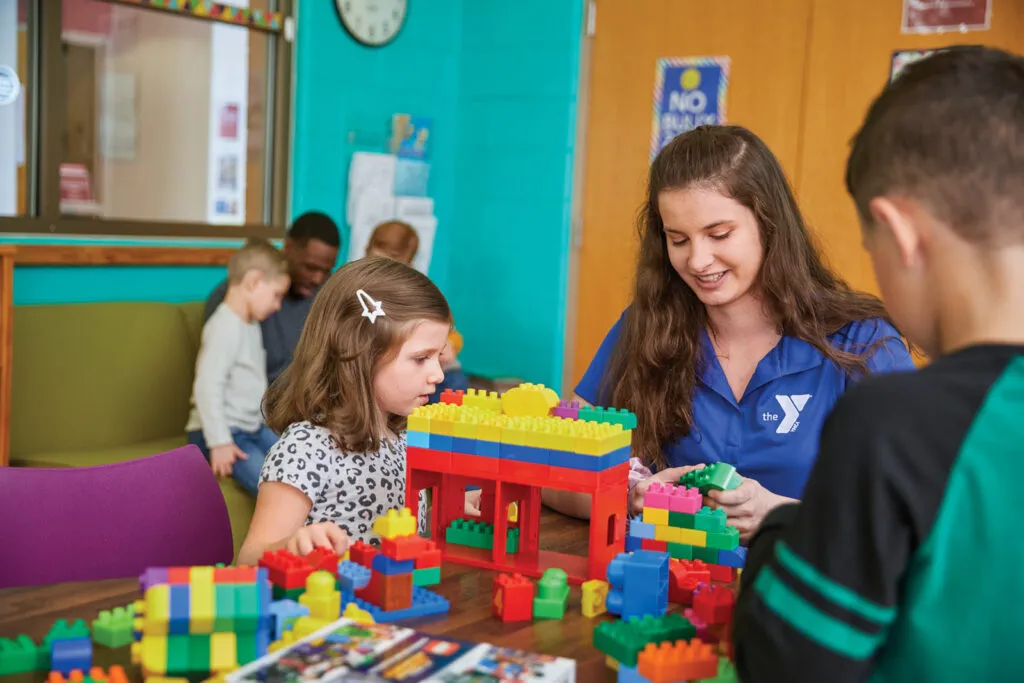 Young girl playing with blocks receives help from team member.