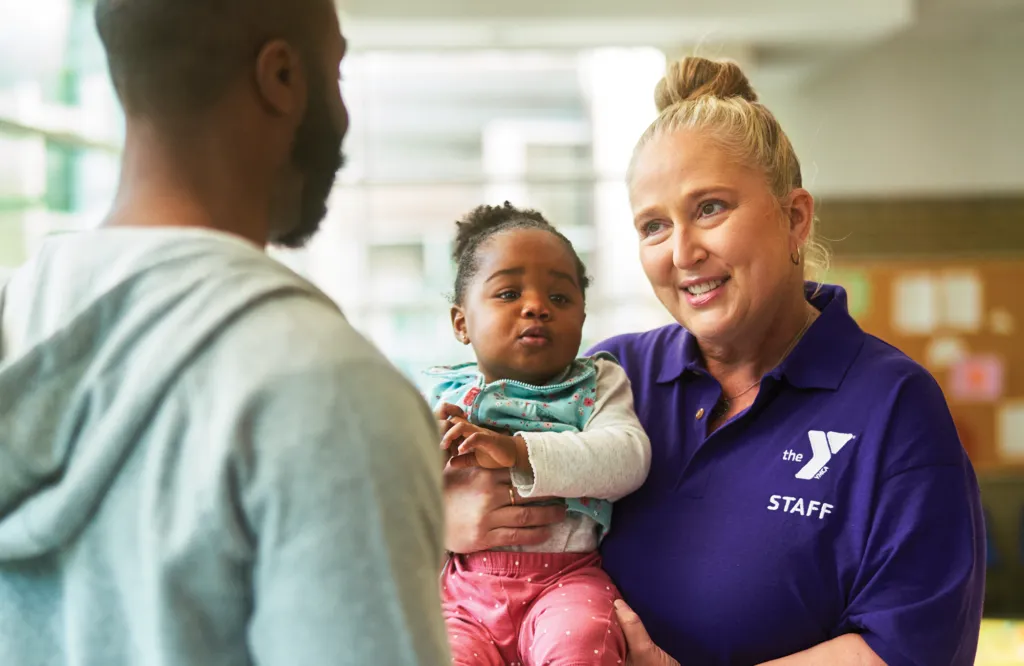 Y team member chats with parent while holding their baby