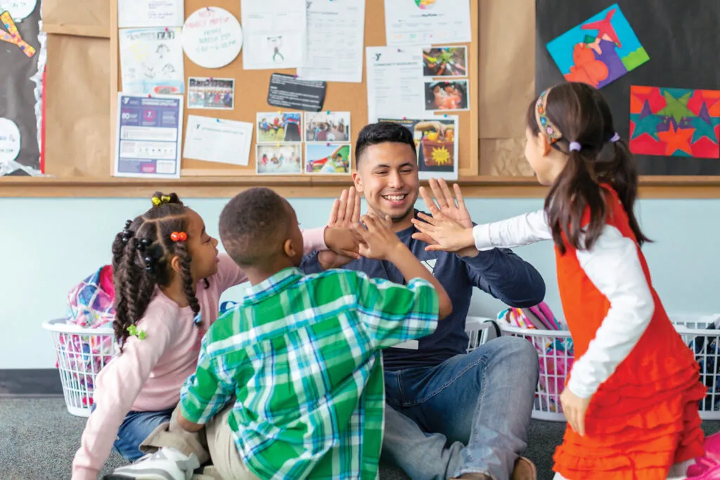 Teacher sits on floor with students, high fiving.