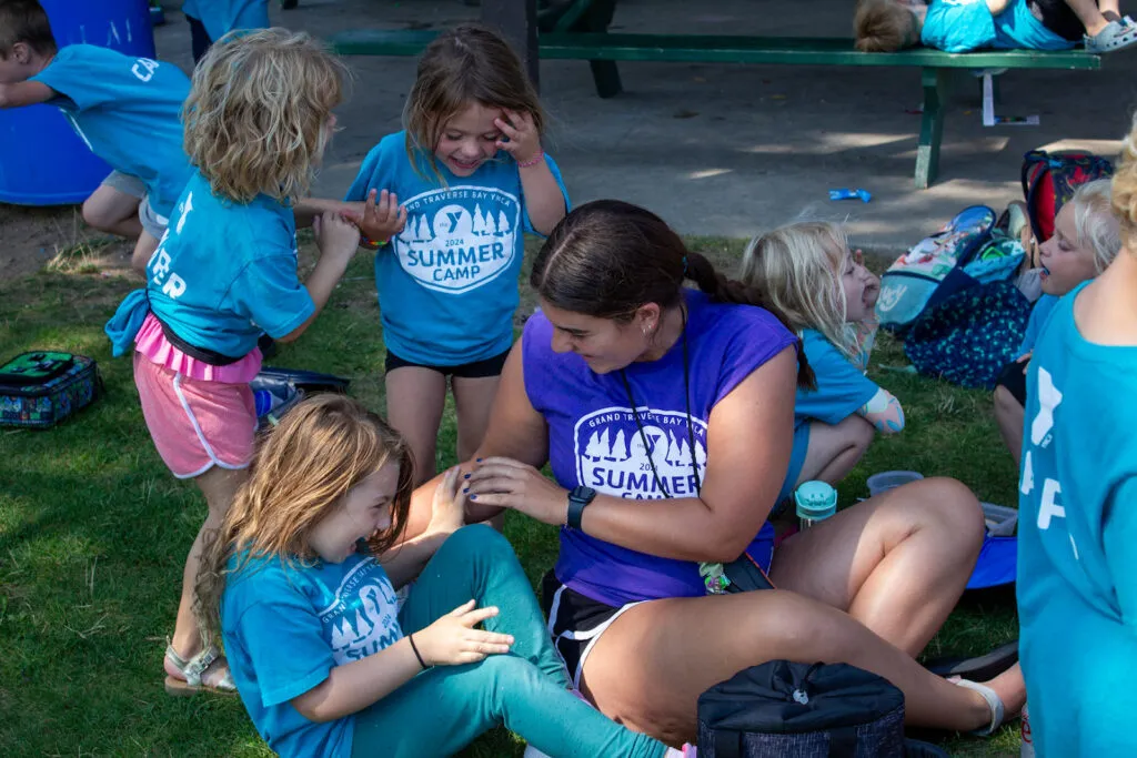 Y team member sits on the grass with giggling children.