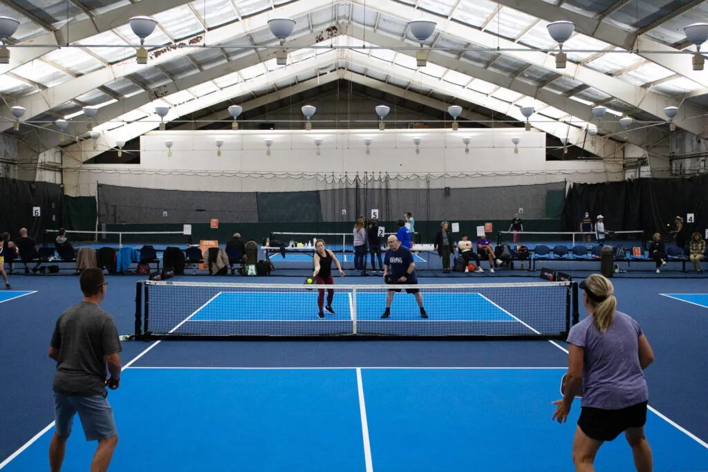 Pickleball game on a blue, brightly lit court.