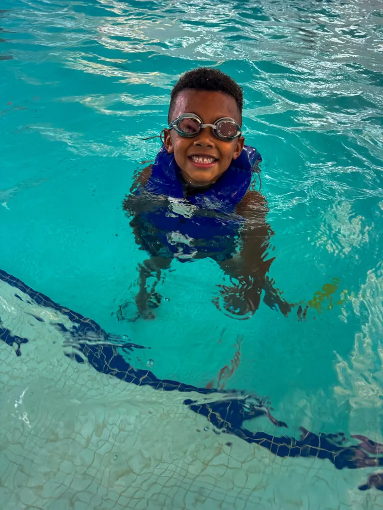 Young child in water safety gear smiles while he floats.
