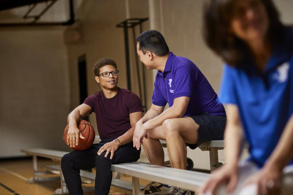 Basketball player sits on bench and chats with coach.