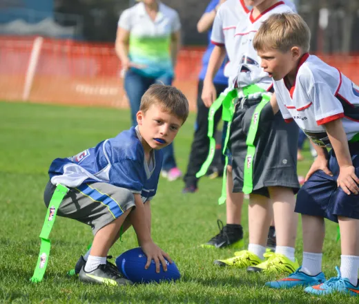 A young boy kneels down, focused on catching a football while playing flag football on the field.