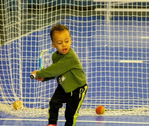 A young boy stands on a tennis court, confidently holding a tennis racket, ready to play.