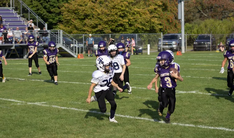 Children playing football chase player in purple, carrying the ball.