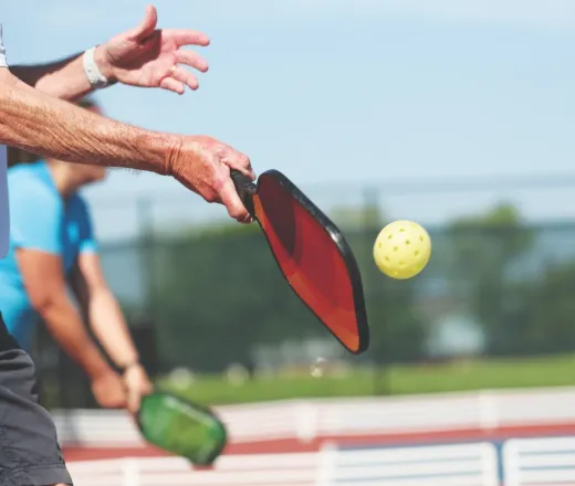 A senior man hits a pickleball with a racket, demonstrating his skill and focus on the court.
