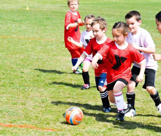 Several kids engaged in a lively soccer game on a sunny field, showcasing teamwork and enthusiasm.