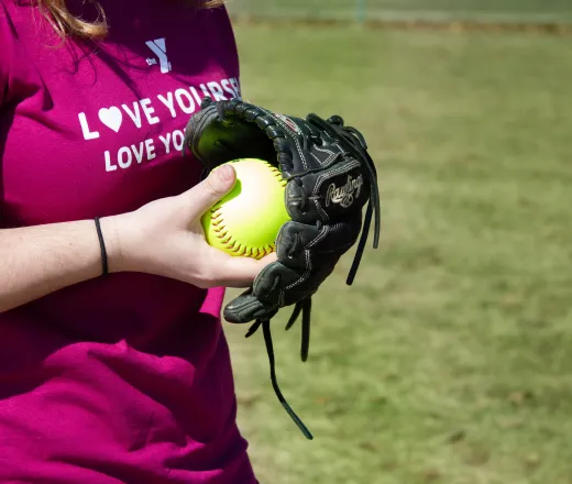A woman wearing a pink shirt grips a baseball glove, showcasing her enthusiasm for softball.