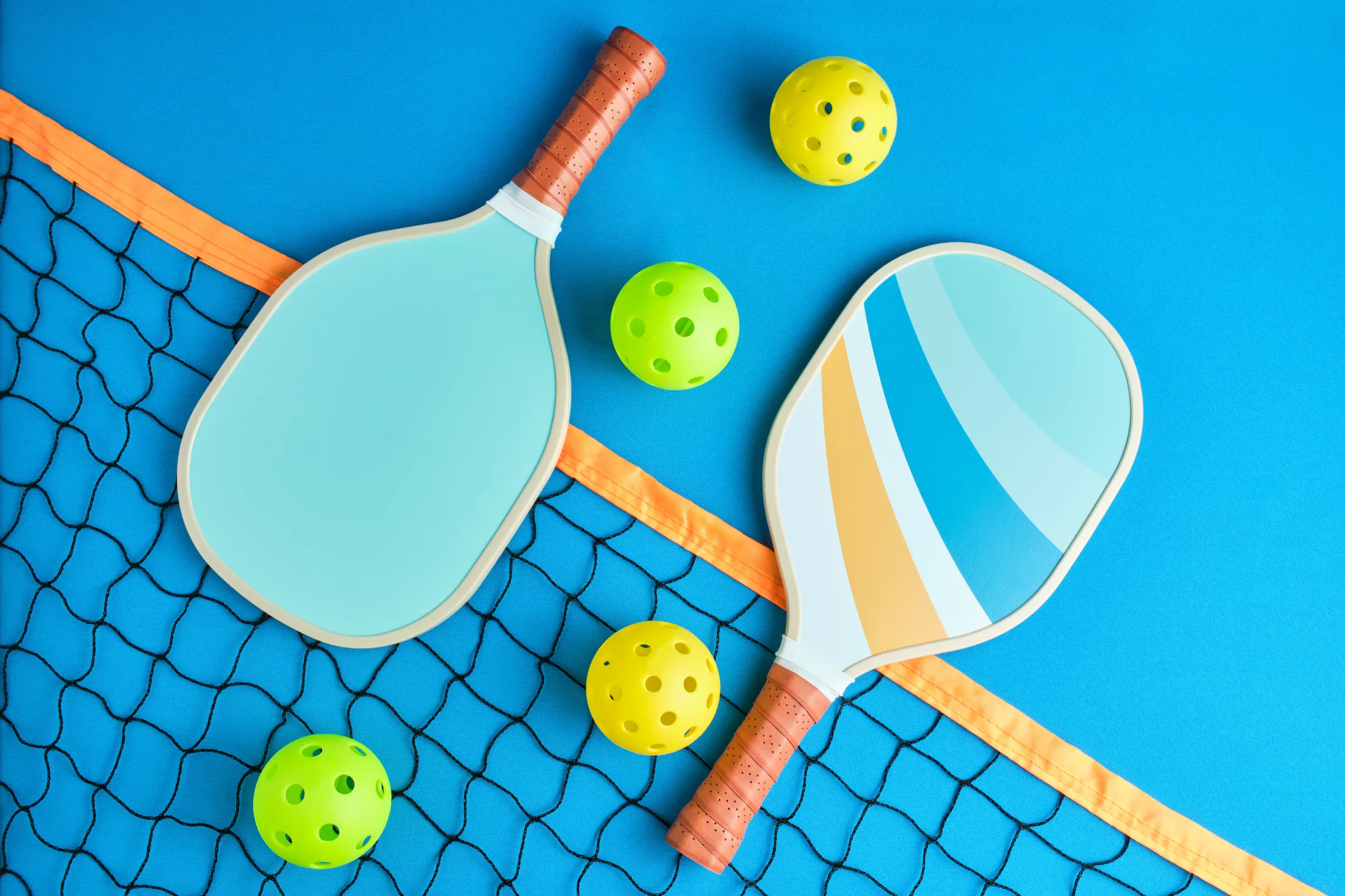 pickleball paddles and balls laying on court on top of net