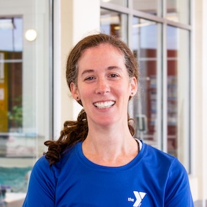 Portrait of woman with dark curly hair wearing a blue YMCA uniform shirt, smiling warmly at camera